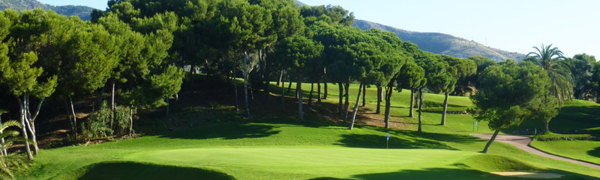 the image is of a golf green surrounded by bunkers with mountains and trees in the background